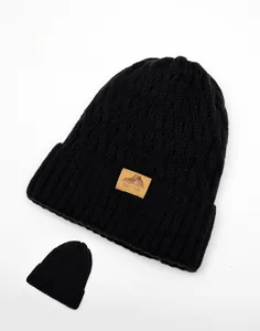 Detailed view of black cable knit beanie featuring thick texture and brown leather logo patch