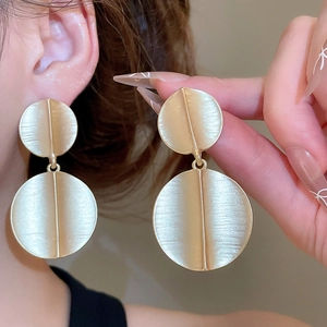 Close-up of matte gold geometric round drop earrings with brushed metal texture