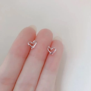 Detailed view of silver heart-shaped crisscross stud earrings held in hand