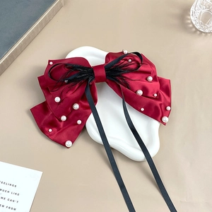 Detail of burgundy satin bow hair clip with white pearls and black feather accents