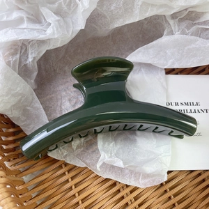 Close-up of a large dark green curved claw clip on white paper inside a basket