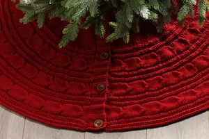 Detail of red cable knit Christmas tree skirt with wooden buttons on wooden floor