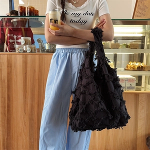Detail of a large black fringe tote bag showing the unique woven texture and fabric tassels