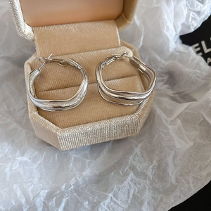 Detail view of irregular silver hoop earrings with matte texture on a beige jewelry box