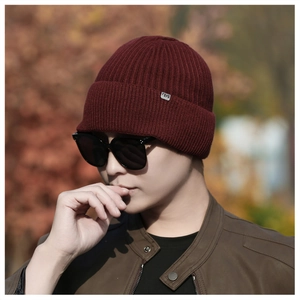 Close-up of burgundy ribbed knit beanie featuring a small metallic brand logo plate