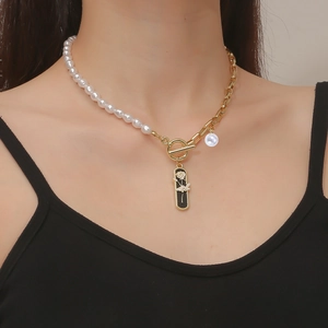 Detailed view of asymmetric necklace with pearls, gold chain, and black rose enamel pendant
