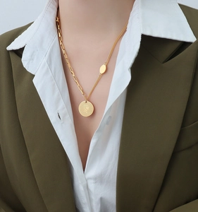 Close-up of asymmetric gold necklace with Elizabeth II coin pendant on green blazer