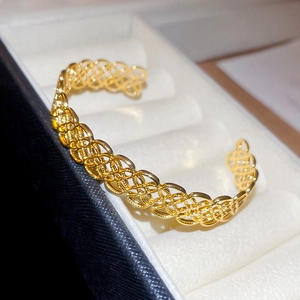 Gros plan sur un bracelet manchette doré ajouré avec texture tissée dans un écrin à bijoux