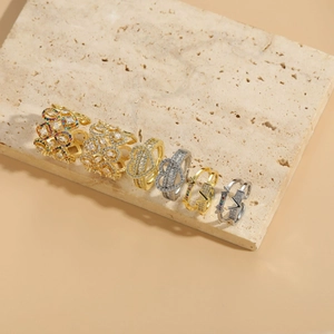 Six bagues géométriques or et argent avec zircons sur une dalle de pierre beige