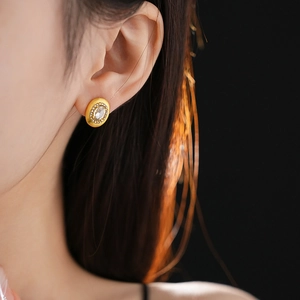 Close-up of golden oval stud earring with rhinestones worn by a model on dark background
