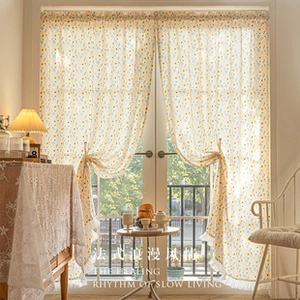 Detail of sheer yellow floral lace curtains with ruffled edges in a warm sunlit room