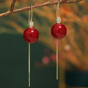 Detail of red globe pearl tassel earrings with golden chain on a natural branch