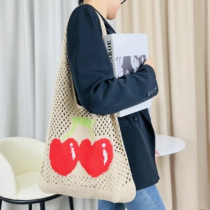 Detail of knitted beige tote bag with red cherry patterns and crochet texture finish