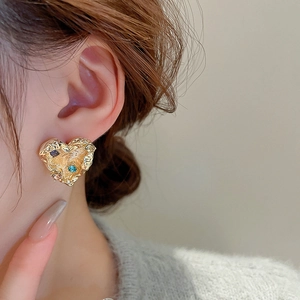Close-up of gold heart earring with lava texture and colorful inlaid crystals