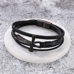 Close-up of a multi-layer black braided leather bracelet with a metal cross charm