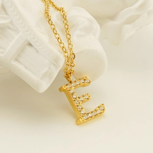 Macro shot of gold-plated letter E pendant with sparkling rhinestones on chain