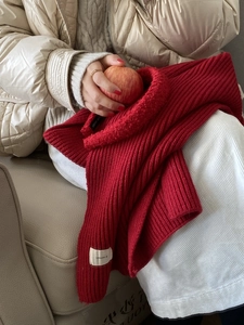 Close-up of a red chunky knit scarf featuring a white woven textile brand label