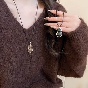 Detail of brown and black leather gourd pendants on a long necklace worn by a model