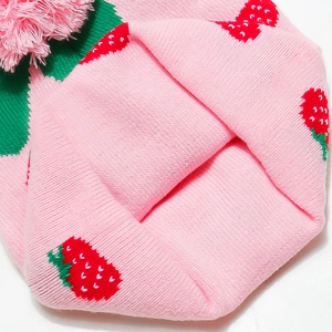 Close-up of pink knit hat showing strawberry pattern detail and soft pompom texture