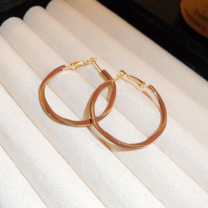 Close-up of twisted round earrings with brown enamel and gold finish on a jewelry tray