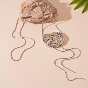 Collier argenté aux textures ondulées et chaîne serpent présenté sur une pierre brute