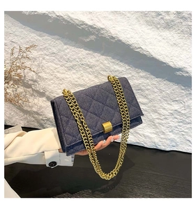 Detail of dark blue denim shoulder bag featuring a gold chain strap and square buckle