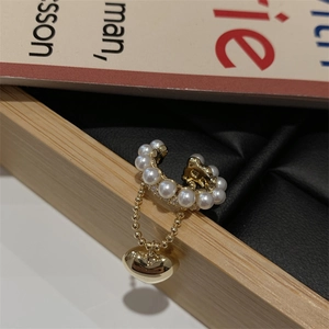 Dettaglio di ear cuff dorato con perle e ciondolo a cuore su catenine di perline