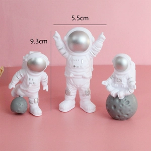 Three astronaut cake toppers with silver visors and height measurements on pink background