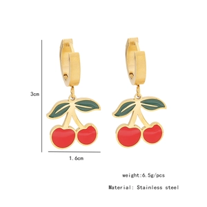 Gros plan de boucles d'oreilles en acier doré avec pendentifs cerise rouge et feuille