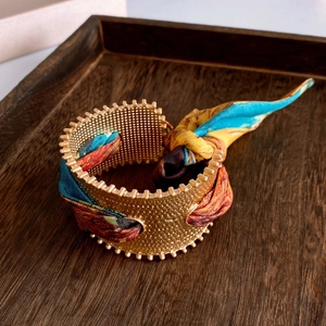 Macro shot of matte gold wide cuff with textured surface and colorful silk weave detail