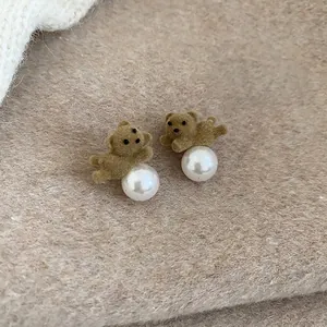 Close-up of brown flocked bear earrings with white pearls on a soft plush backdrop