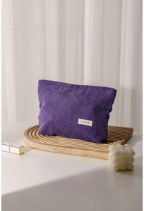 Detail of purple corduroy makeup bag with H&R label on a wooden tray with soft lighting