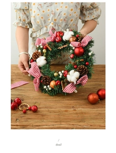 Detail showing a Christmas wreath with pine cones and plaid bow on a rustic wooden table