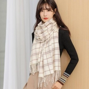Close-up of soft beige plaid scarf with tassel fringe worn by a model in winter