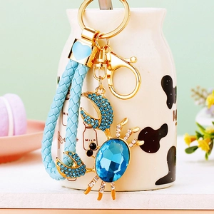 Close-up of golden crab keychain featuring large blue crystals and woven leather strap