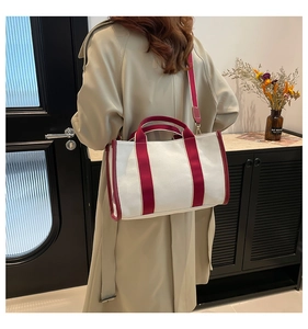 Canvas tote bag with burgundy trim shown on a model in a stylish beige trench coat