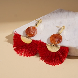 Dettaglio di orecchini bohémien con nappe rosse, dettagli dorati e perline in resina arancio