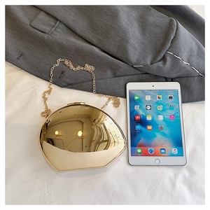 Close-up of golden geometric evening clutch bag with metal chain on white bedding surface
