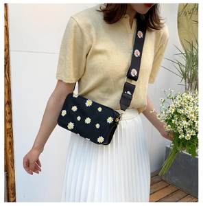 Detailed view of black daisy print crossbody bag with matching wide strap on a model