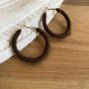 Detailed view of dark brown flocked hoop earrings on a warm wooden surface