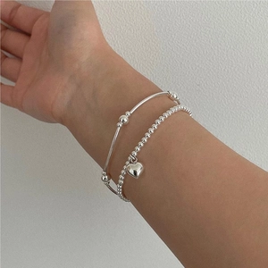 Detail of silver S925 beaded bracelet with heart pendant and minimalist elastic bangles