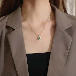 Détail d'un collier doré avec pendentif ovale en pierre verte et micro-diamants sur mannequin