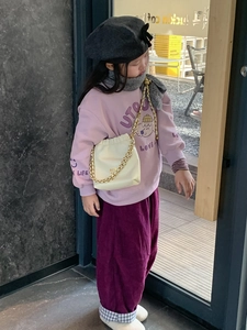 Nahaufnahme einer beigen Kinder-Umhängetasche mit Goldkette und fliederfarbenem Outfit