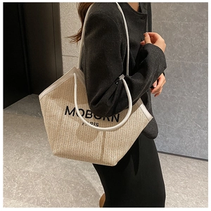 Close-up of woven straw tote bag with MOBORN PARIS lettering and white leather trim