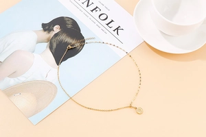 Flat lay of a gold stainless steel coin pendant necklace on a beige aesthetic background