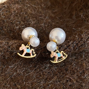 Close-up of pearl stud earrings with pink and blue enamel rocking horse charms