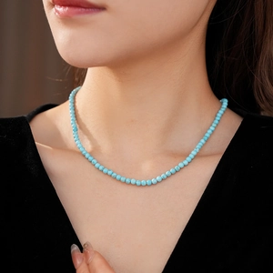 Close-up of minimalist turquoise beaded necklace worn against a black fabric background