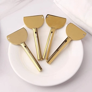 Close-up of four golden metal toothpaste squeezers arranged on a clean white ceramic plate