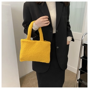 Detail of yellow plush teddy fleece handbag held by a model in a minimalist indoor setting