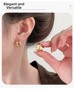 Close-up of square gold metal earrings with a high-polished finish on a model's ear